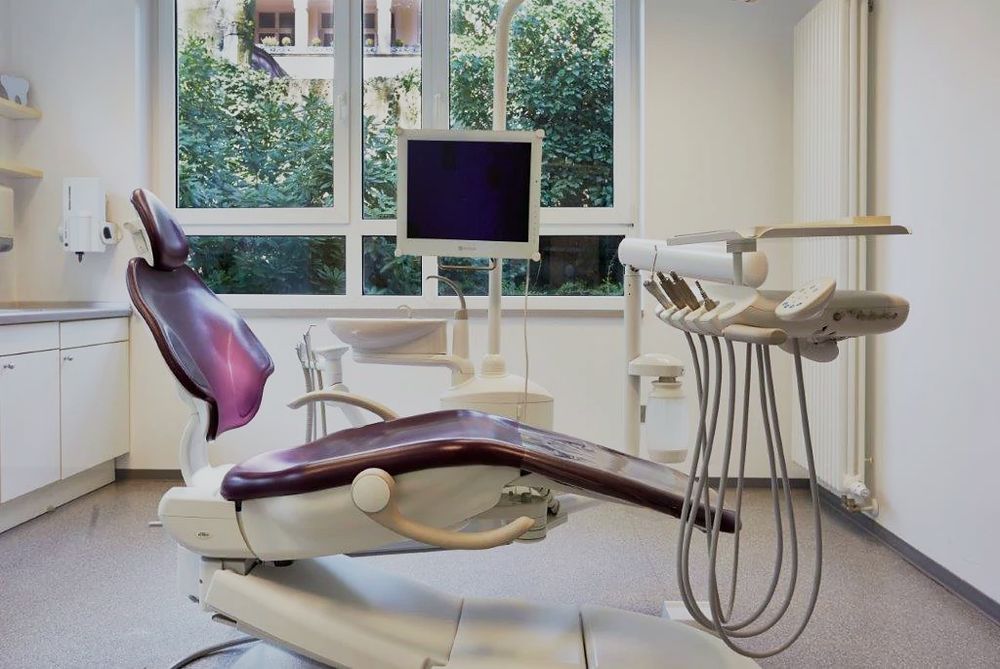 Behandlungszimmer mit Behandlungsstuhl und Bildschirm am Fenster